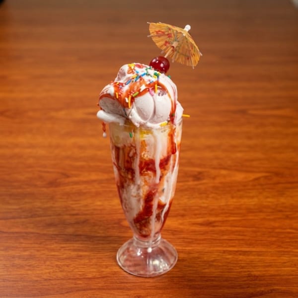A tall glass of ice cream with strawberry syrup, sprinkles, a cherry, and a small umbrella.