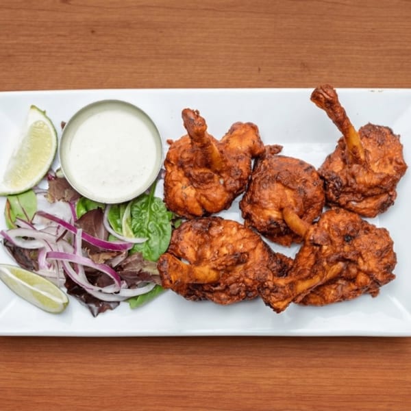 Crispy fried chicken lollipops with a side of salad, lime wedges, and white dipping sauce.