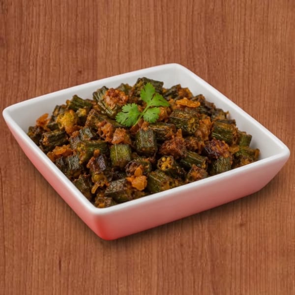Spicy okra curry, garnished with cilantro, served in a white square bowl on a wooden surface.
