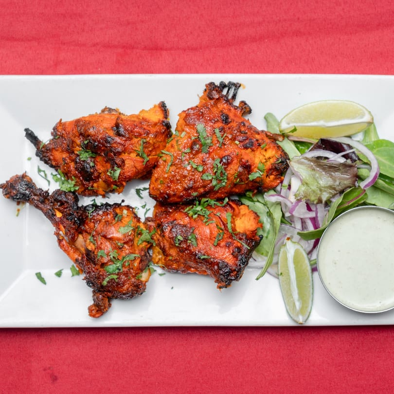 Four pieces of tandoori chicken with cilantro, salad, lime wedges, and a side of green sauce.
