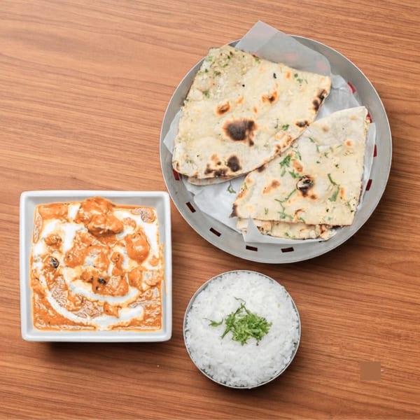 Indian butter chicken, naan bread, and white rice with herbs on a wooden table.