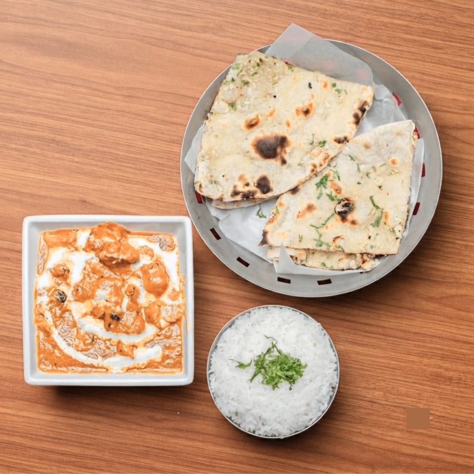 Indian butter chicken, naan bread, and white rice with herbs on a wooden table.