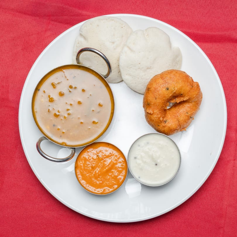 South Indian breakfast with idli, vada, sambar, and two chutneys on a white plate.