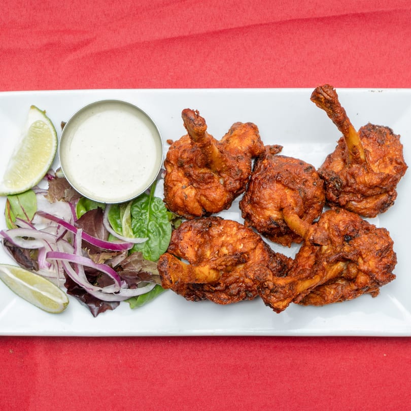 Crispy fried chicken lollipops with a side of salad, lime, and creamy dipping sauce.
