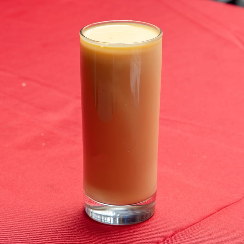 A tall glass of creamy, light brown beverage with a frothy top on a red tablecloth.