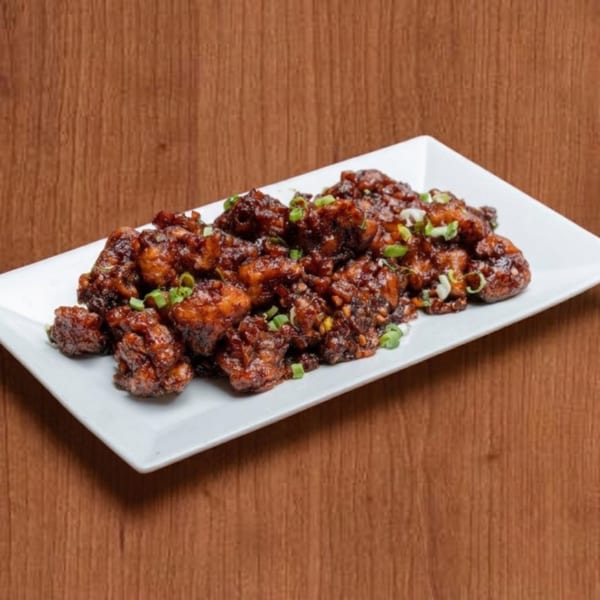 A white rectangular plate filled with dark brown, glazed chicken pieces garnished with chopped green onions.
