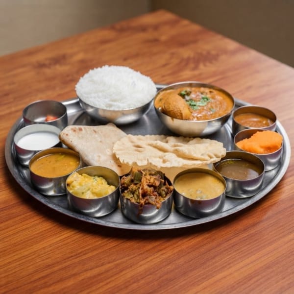 A traditional Indian thali meal with rice, curries, flatbread, and papadum on a metal tray.