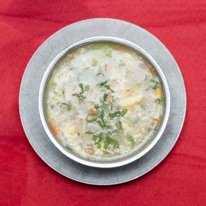 Creamy white soup with vegetables and herbs in a silver bowl on a red tablecloth.