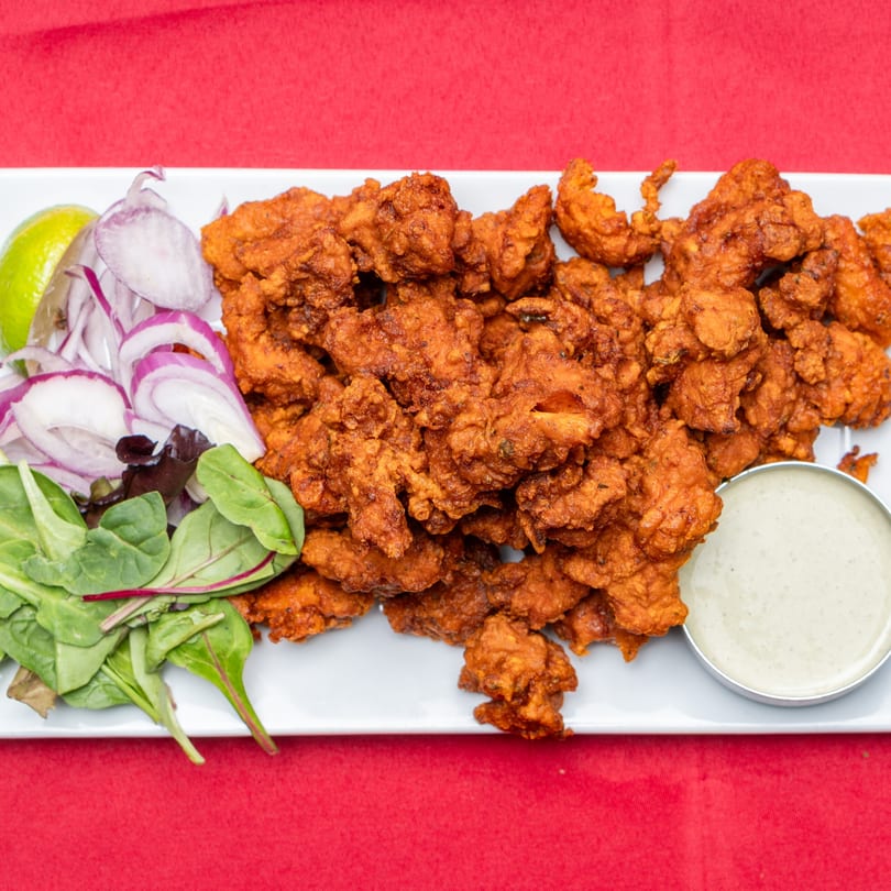 Crispy fried chicken pakora with red onion, lime, mixed greens, and a side of dipping sauce.