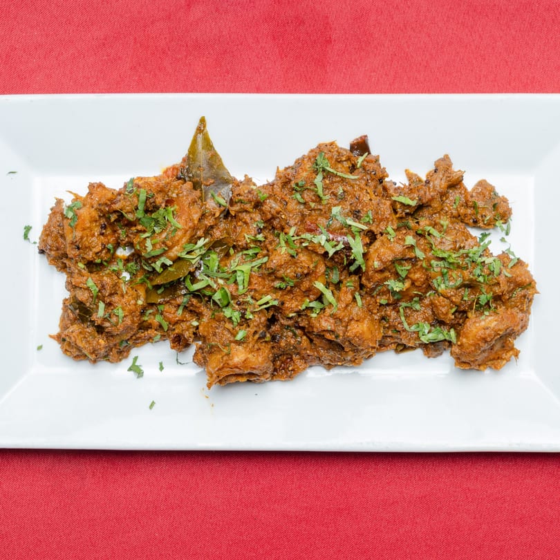 Spicy chicken curry with fresh cilantro and bay leaves on a white rectangular plate.
