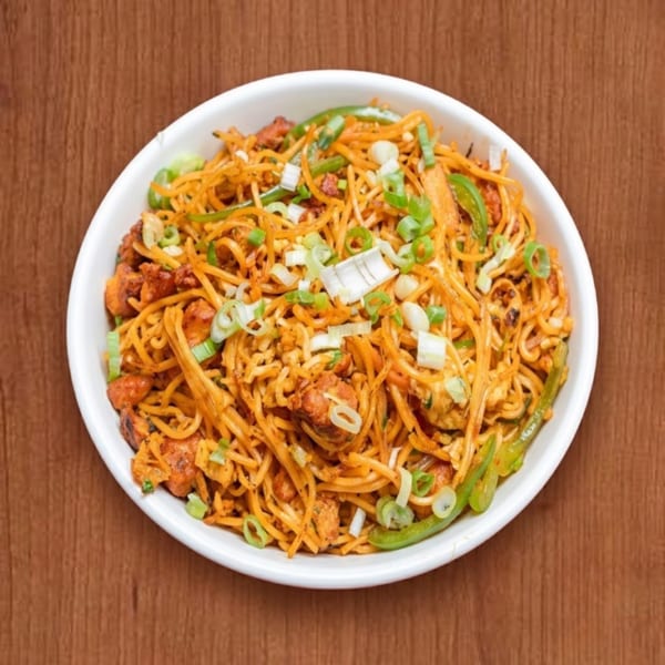 Chicken Hakka Noodles with green peppers and spring onions in a white bowl on a wooden table.