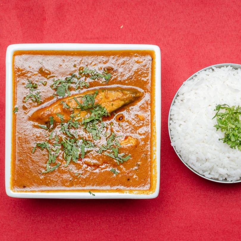A white rectangular dish of fish curry with cilantro, next to a bowl of white rice.