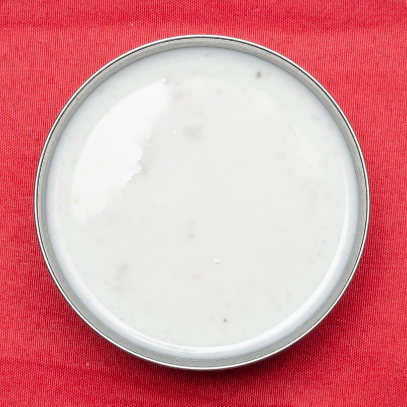Overhead view of a small metal bowl filled with white sauce on a red tablecloth.