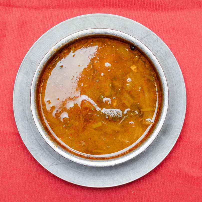 Top-down view of a metal bowl filled with a rich, orange-brown soup on a red tablecloth.